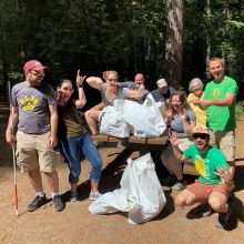 Adults make comical poses around filled bags of litter, in a park.
