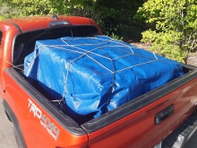 Red truck with a secured load Red 4x4 pickup truck with a full load secured by a blue tarp and ropes.